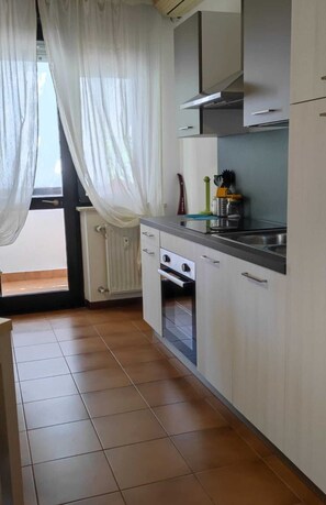 Une cuisine équipée d’une cuisinière, d’un four et d’un évier, avec une fenêtre et des rideaux.
