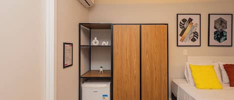 A bedroom with a bed, a wardrobe, a small fridge, and a wall-mounted air conditioner.
