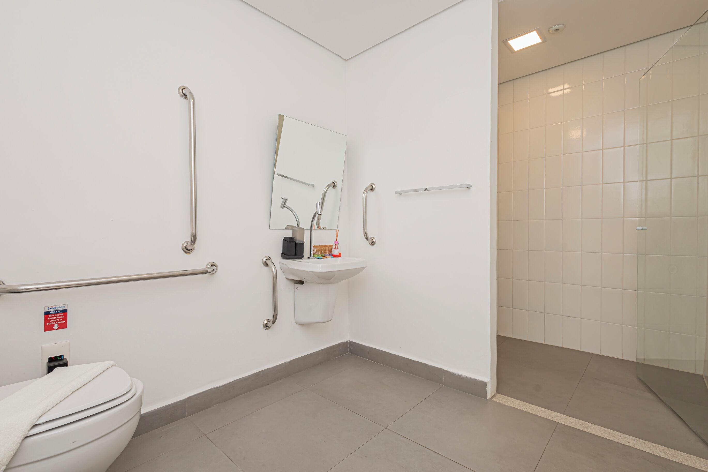 Et badeværelse med toilet, vask, spejl og gelænder.