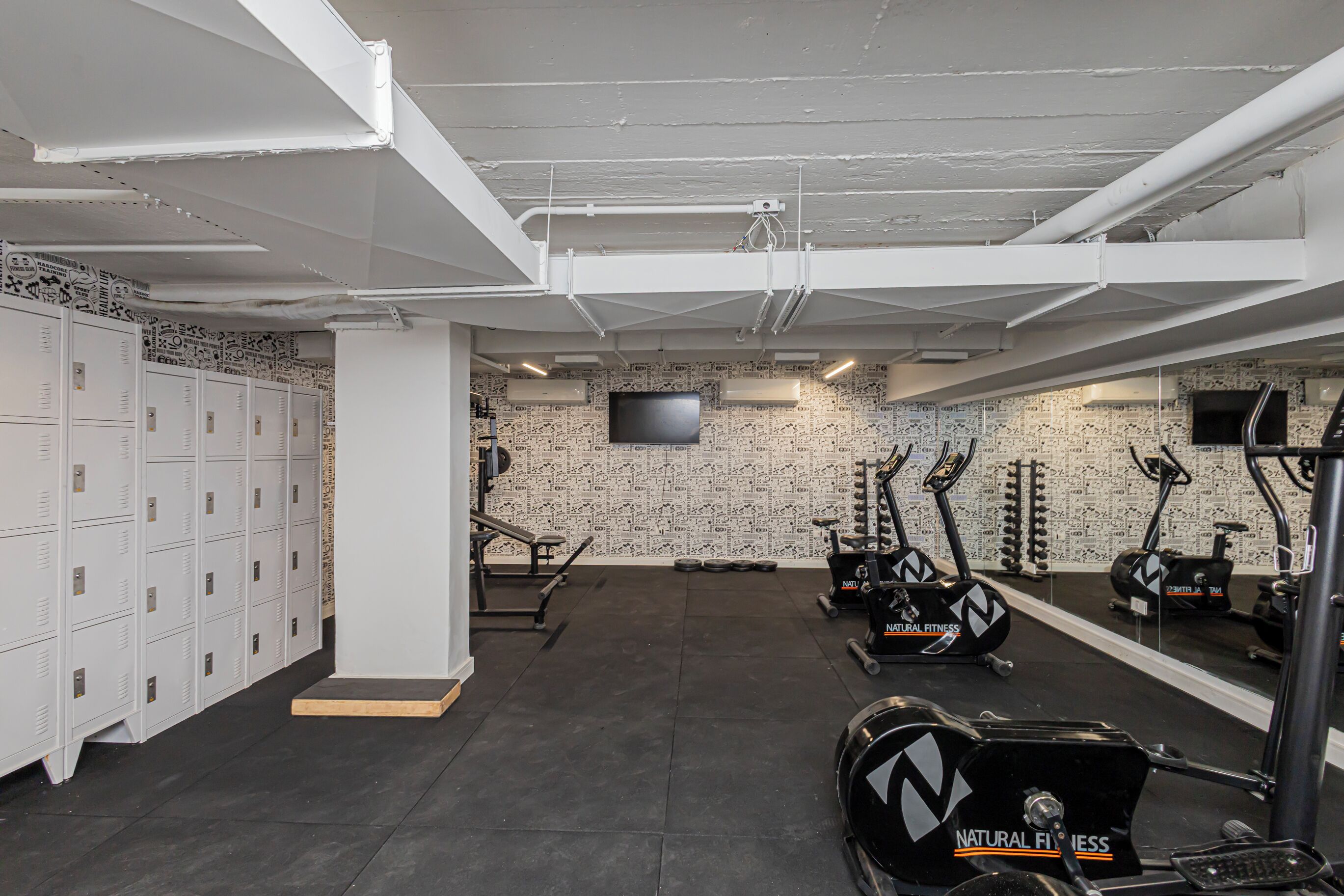 A gym with exercise equipment, lockers, and a mirrored wall.