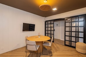 A modern room with a round wooden table, four chairs, a television on the wall, and a sliding door with a grid pattern. - One House by Anora Spaces (São Paulo)