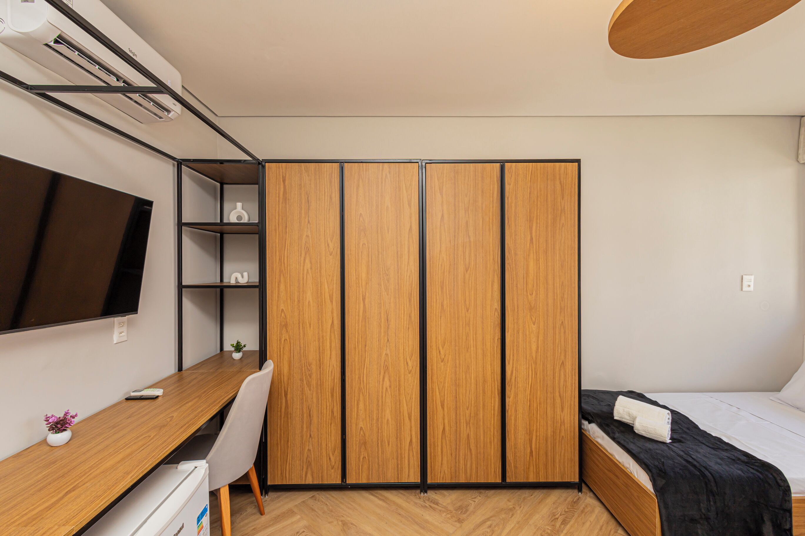 Ein Schlafzimmer mit Bett, Schreibtisch, Fernseher und Kleiderschrank.