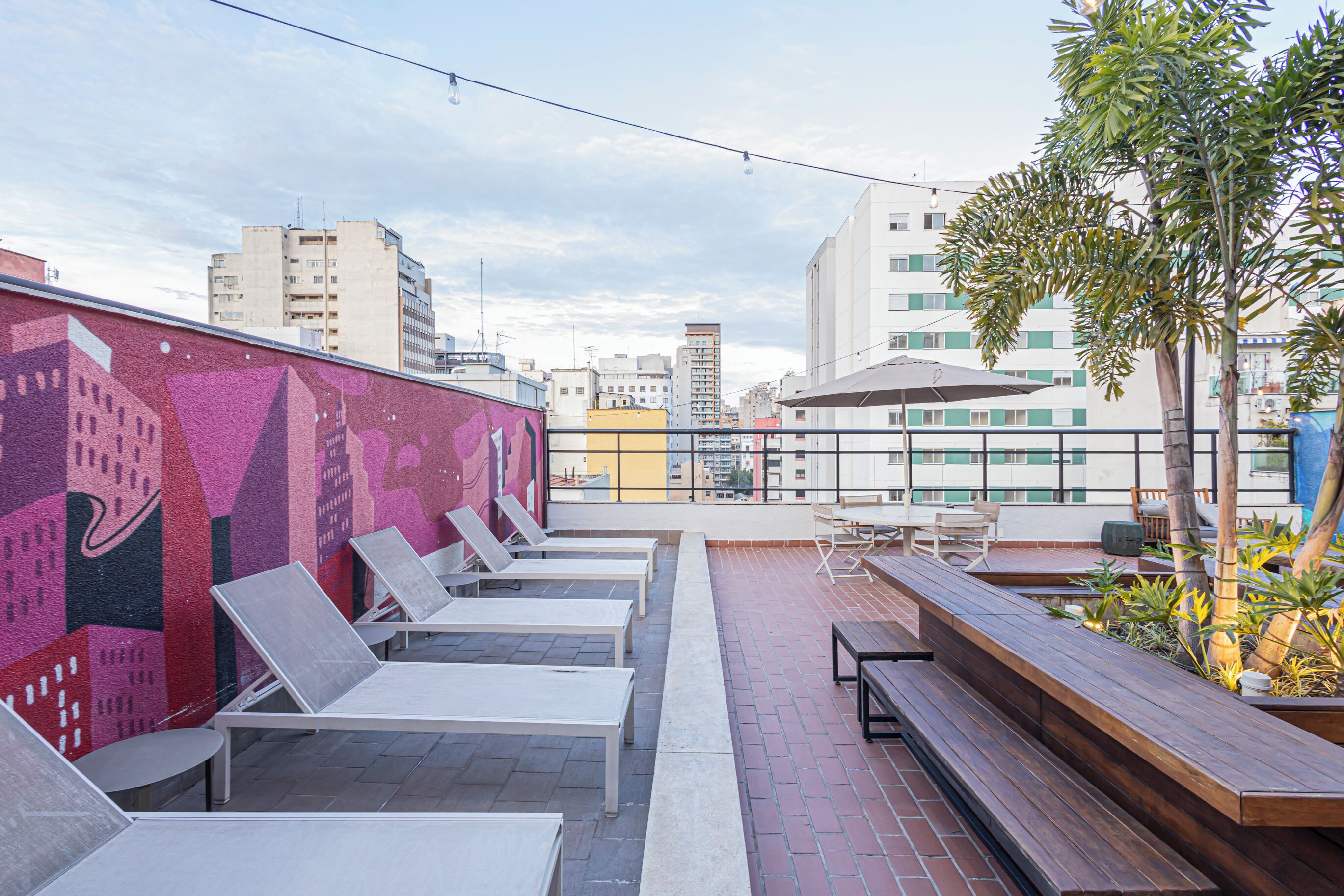 Een terras op het dak met lounge stoelen, een houten bank en een muurschildering.