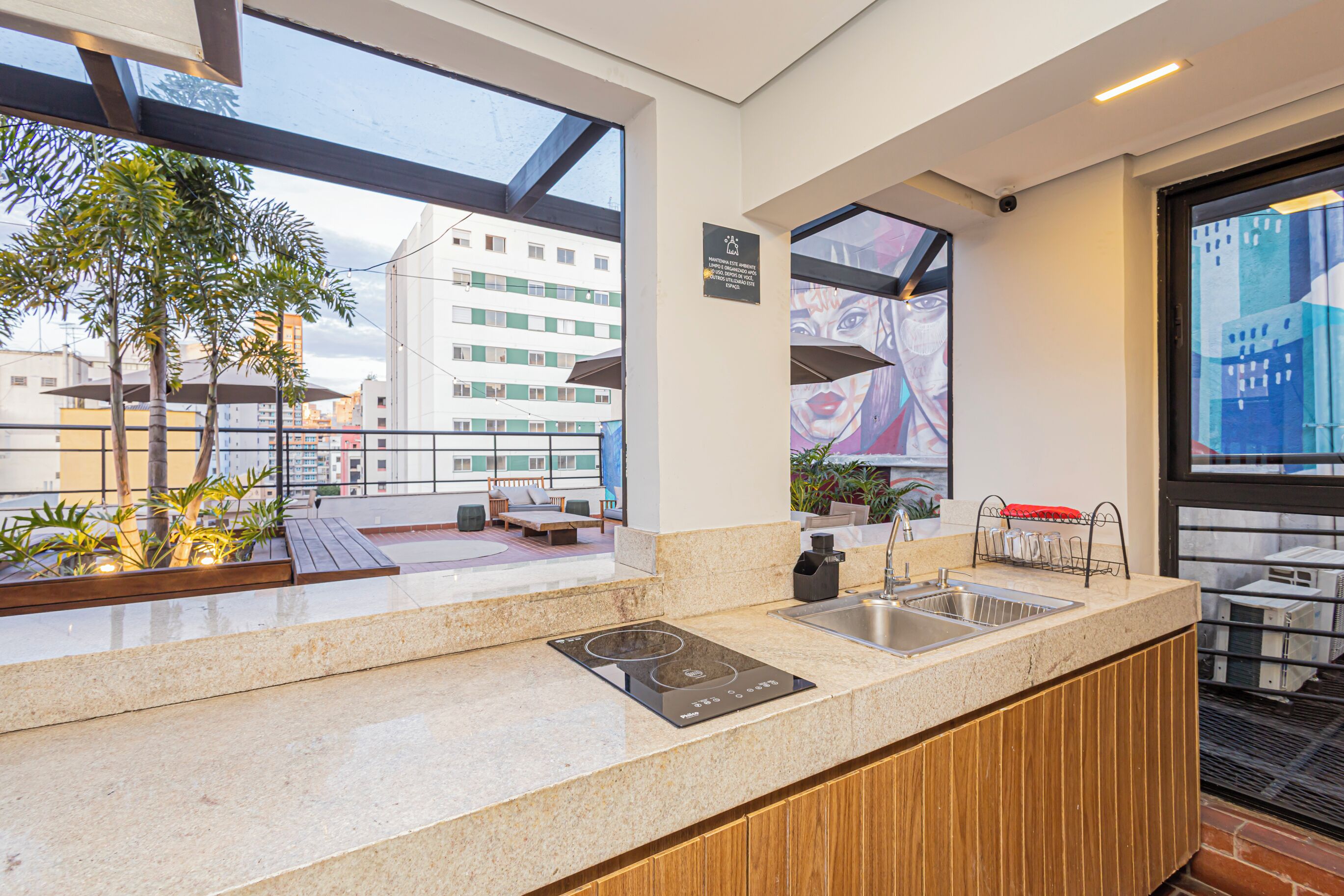 A modern kitchen with a built-in stove, sink, and a view of the cityscape through large windows.