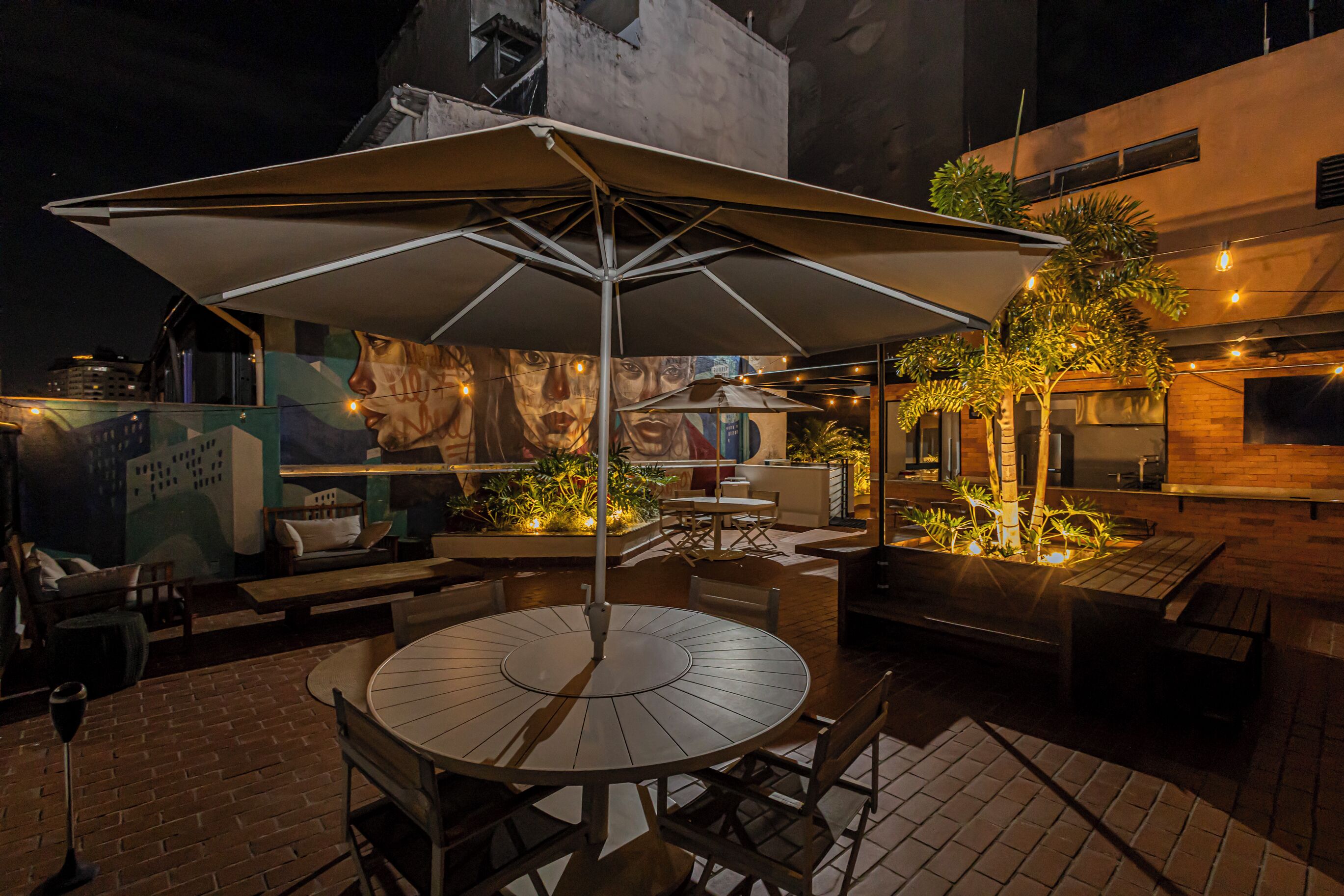 An outdoor dining area with a round table and chairs, an umbrella, and a mural on the wall.