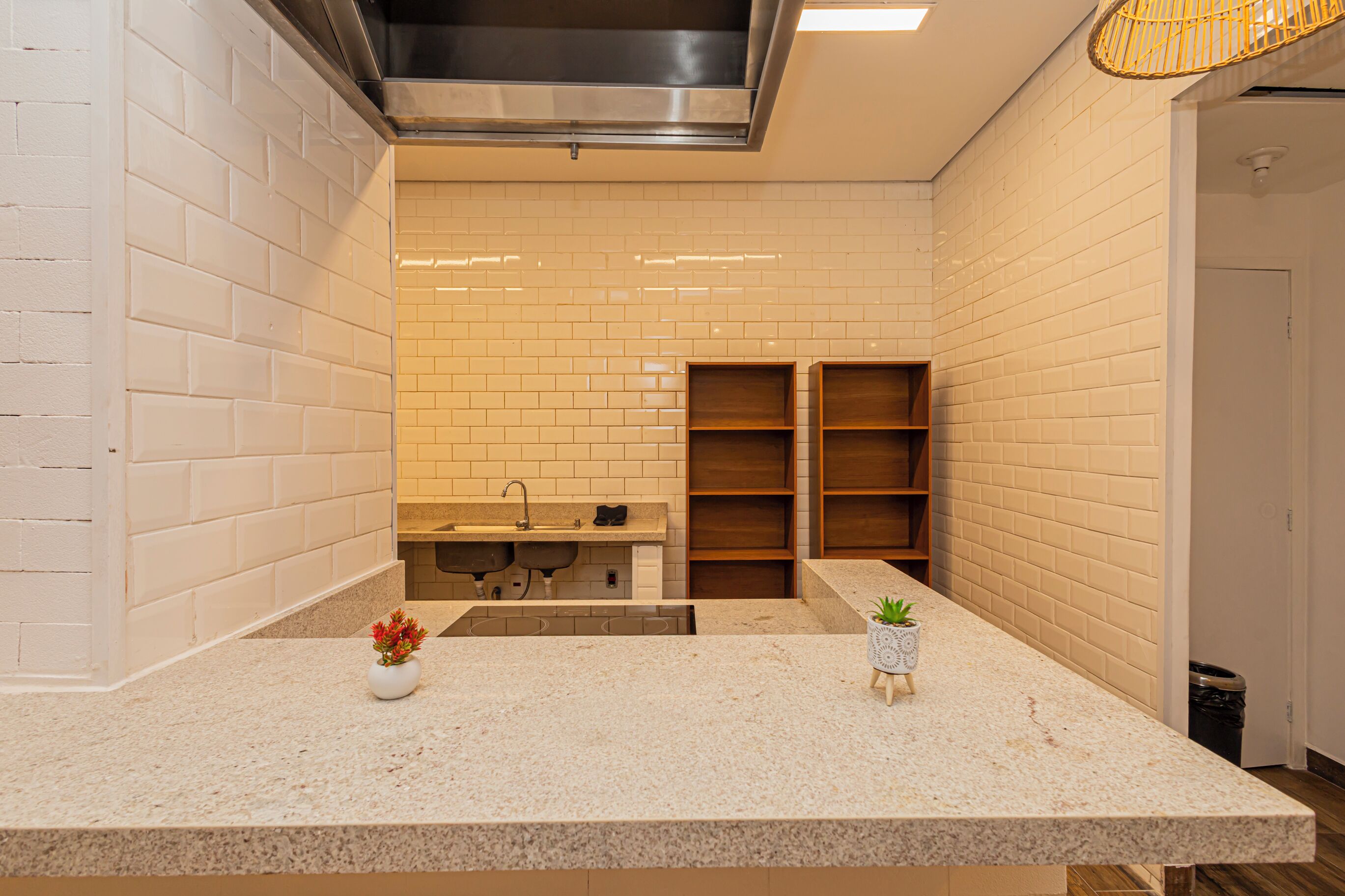 Une cuisine moderne avec des carreaux de céramique blancs disposés en motif métro, une hotte en acier inoxydable, un évier avec un robinet et des étagères en bois.