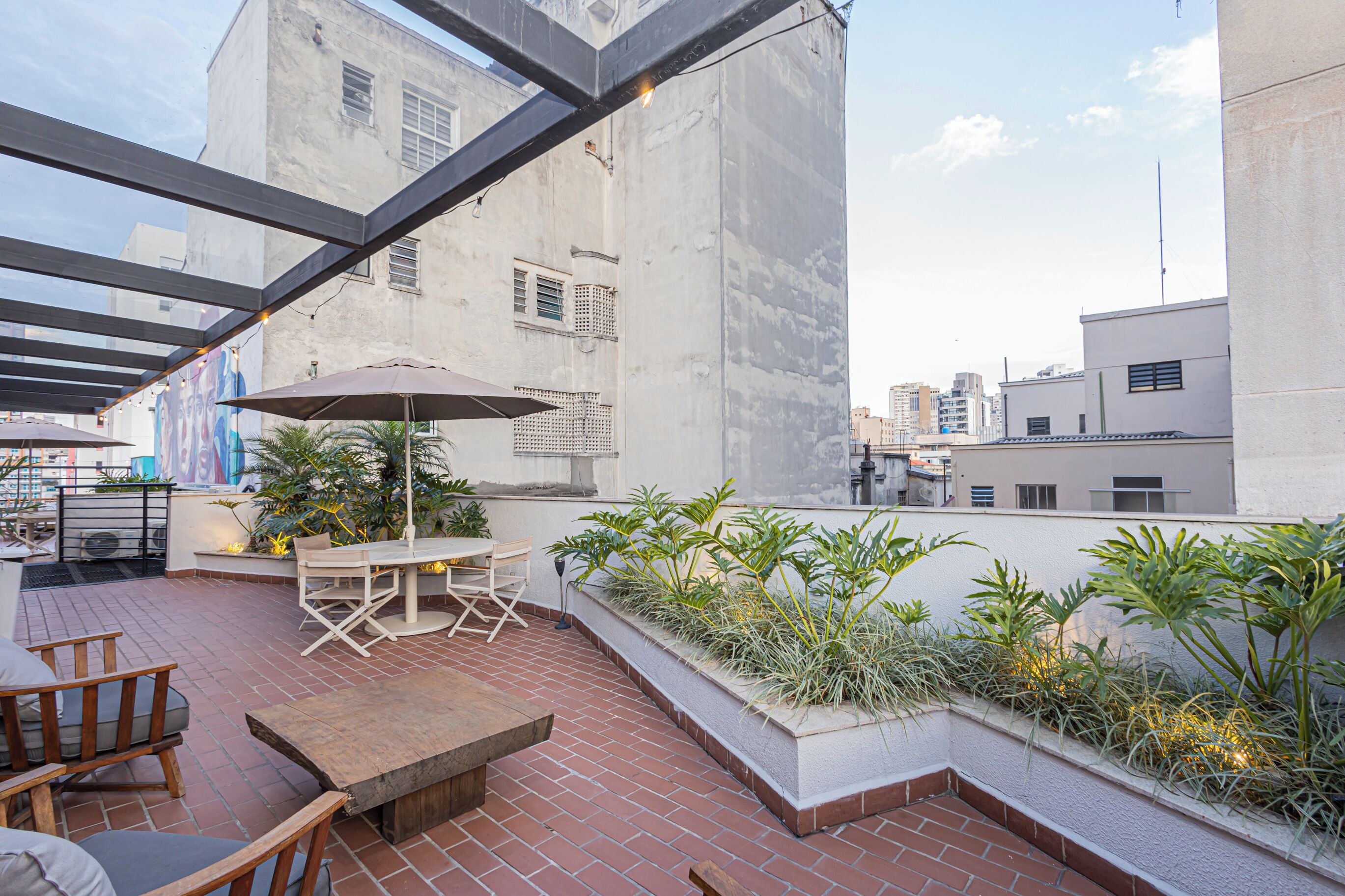 Un patio al aire libre con una mesa y sillas, rodeado de plantas y vistas de la ciudad.