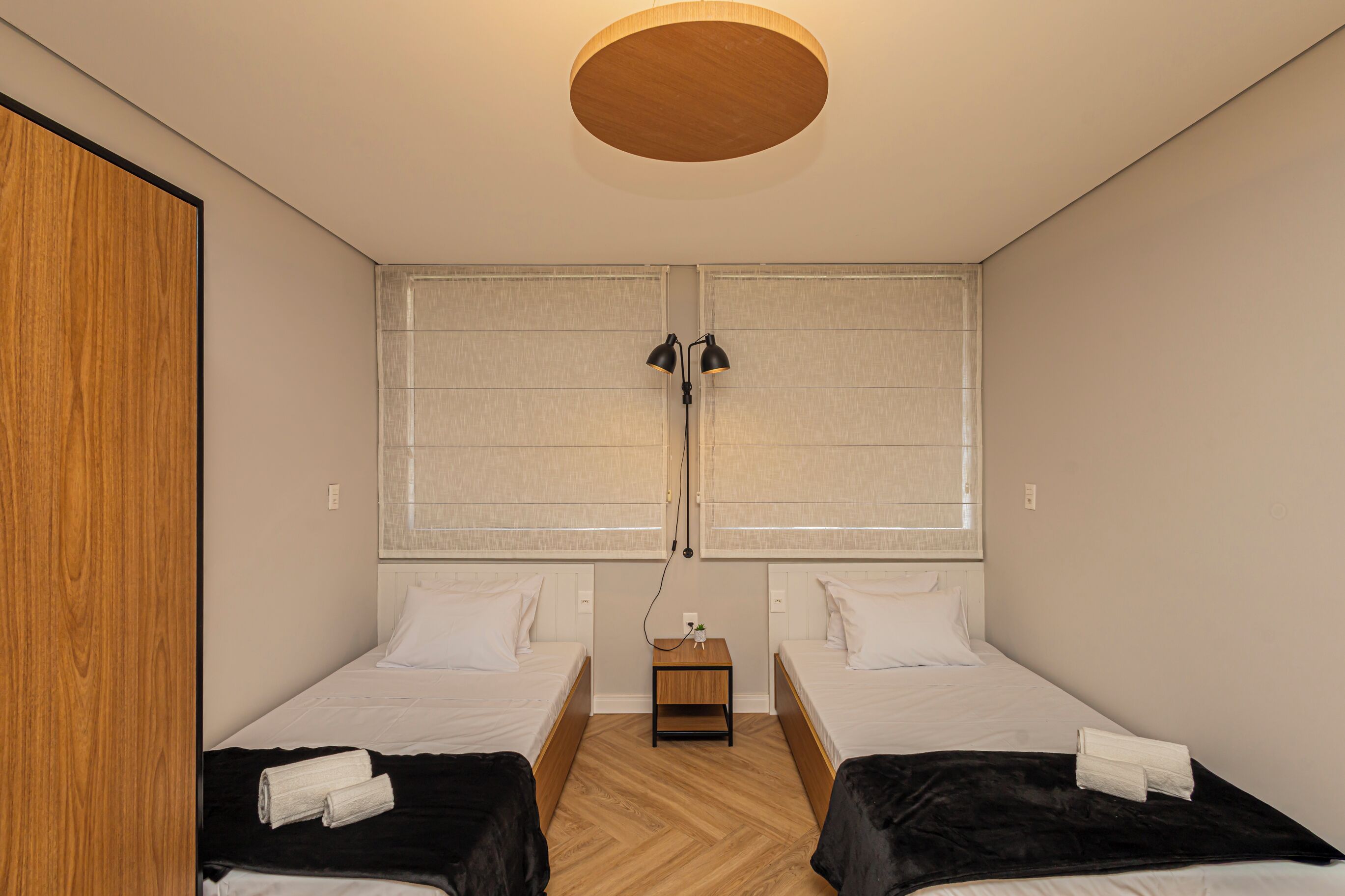 Une chambre avec deux lits, une armoire en bois, une petite table avec une lampe et un luminaire au plafond.