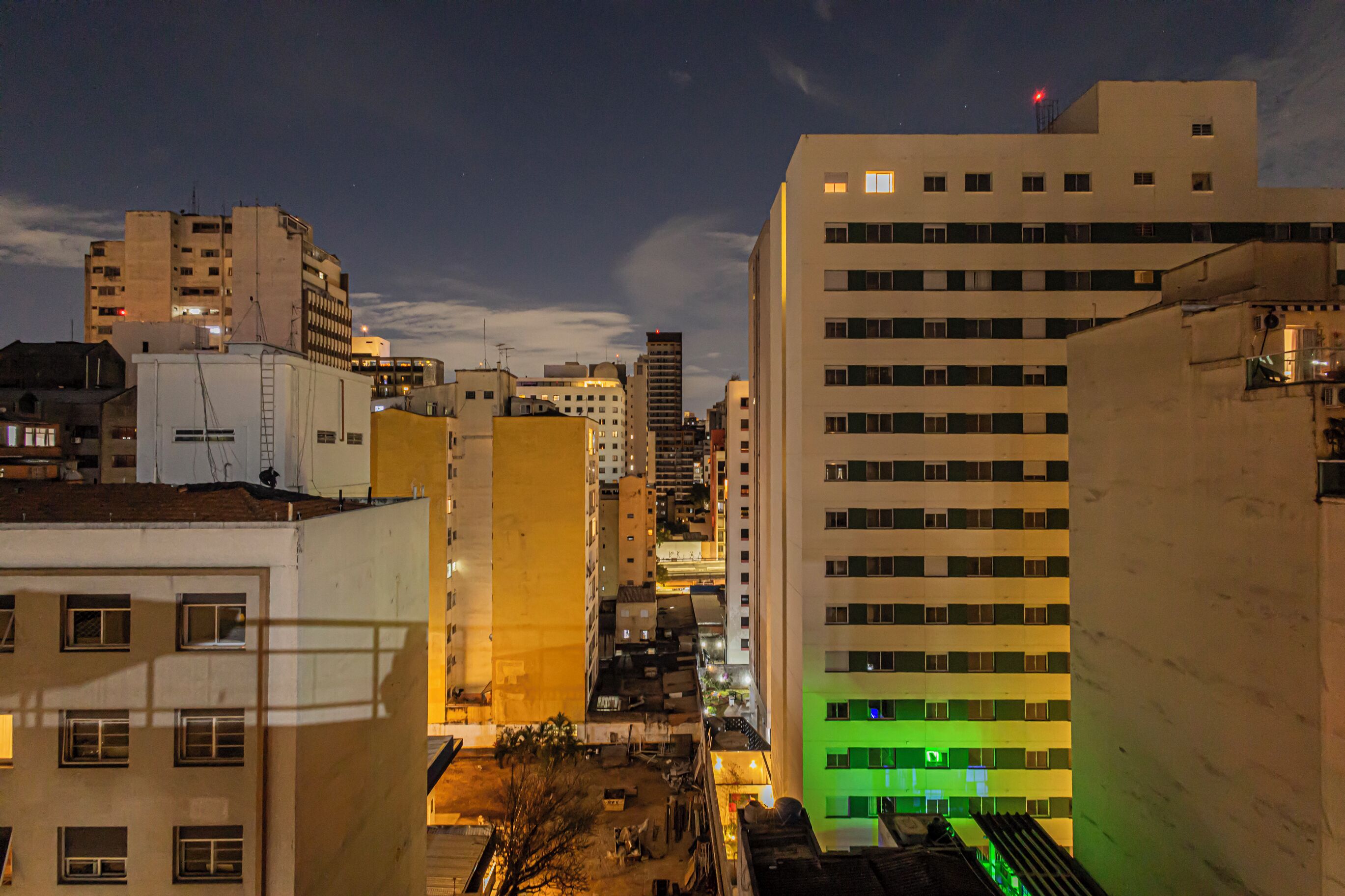 A nighttime cityscape with high-rise buildings, one with a green-lit facade.