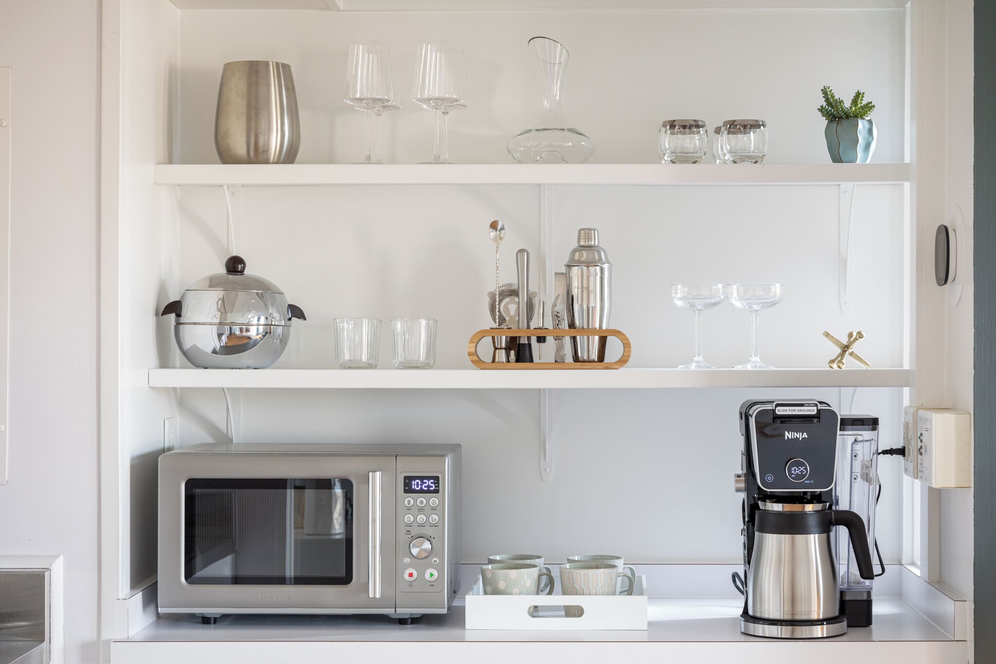 Una cocina equipada con microondas, cafetera y estantes con cristalería y utensilios de cocina.