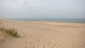 Platja sorrenca amb vegetació escassa i mar tranquil sota un cel ennuvolat.