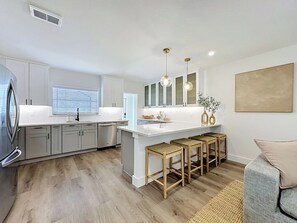 Une cuisine moderne avec des meubles blancs, un îlot central et des tabourets de bar.