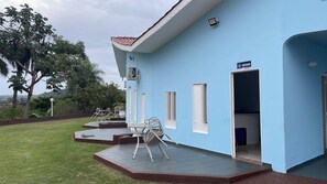 A light blue building with a reception area, outdoor seating, and a view of the surrounding landscape. - POUSADA SHOPPING DO SONO LTDA (Jaciara)