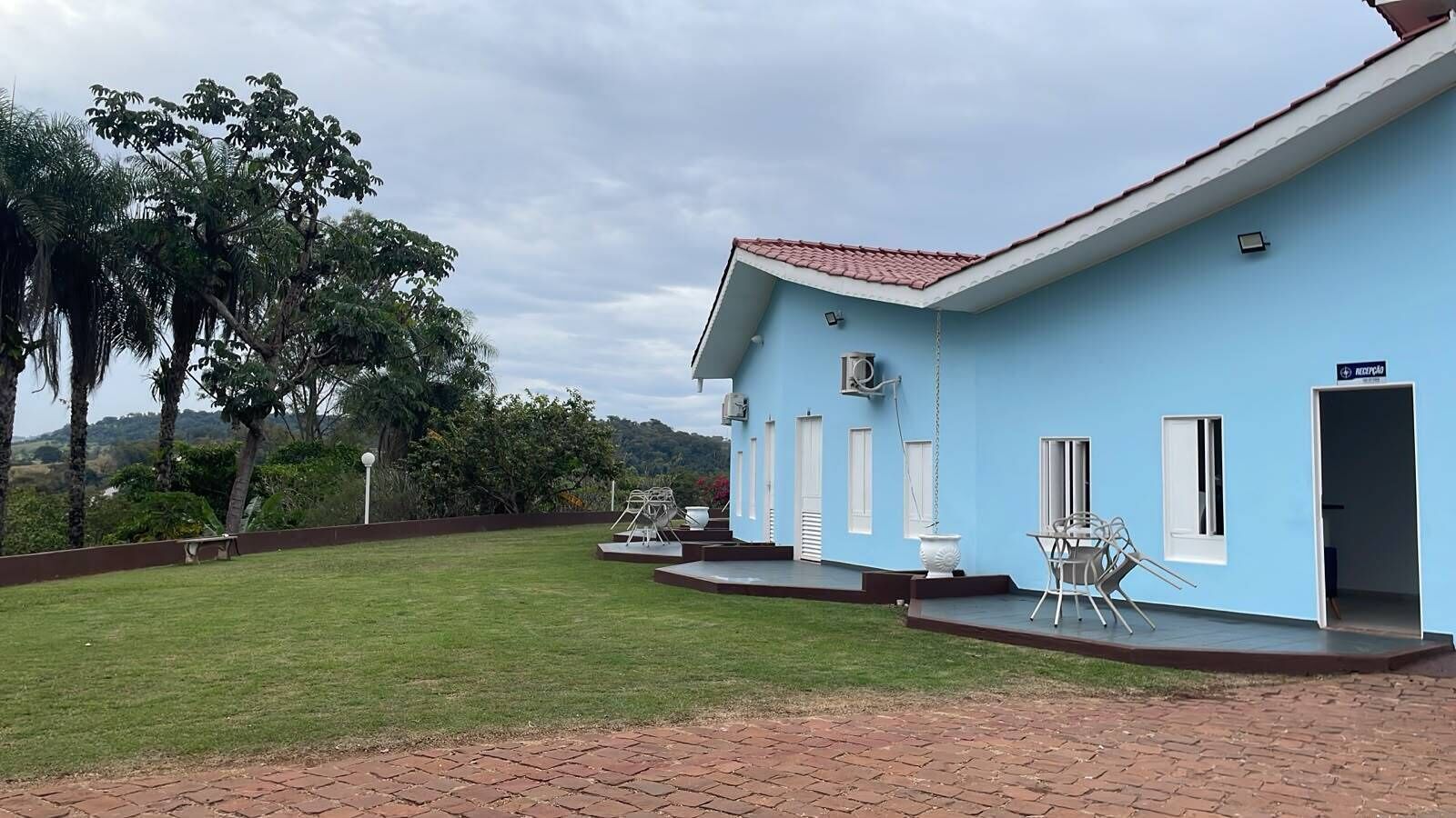 Un bâtiment de couleur bleu clair, avec un toit rouge, une terrasse dallée et une pelouse verdoyante.