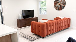 Un salon moderne avec un canapé d’angle, un téléviseur à écran plat et un grand tableau abstrait accroché au mur.
