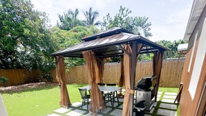 Un patio couvert équipé d’un barbecue, de chaises et d’une table.