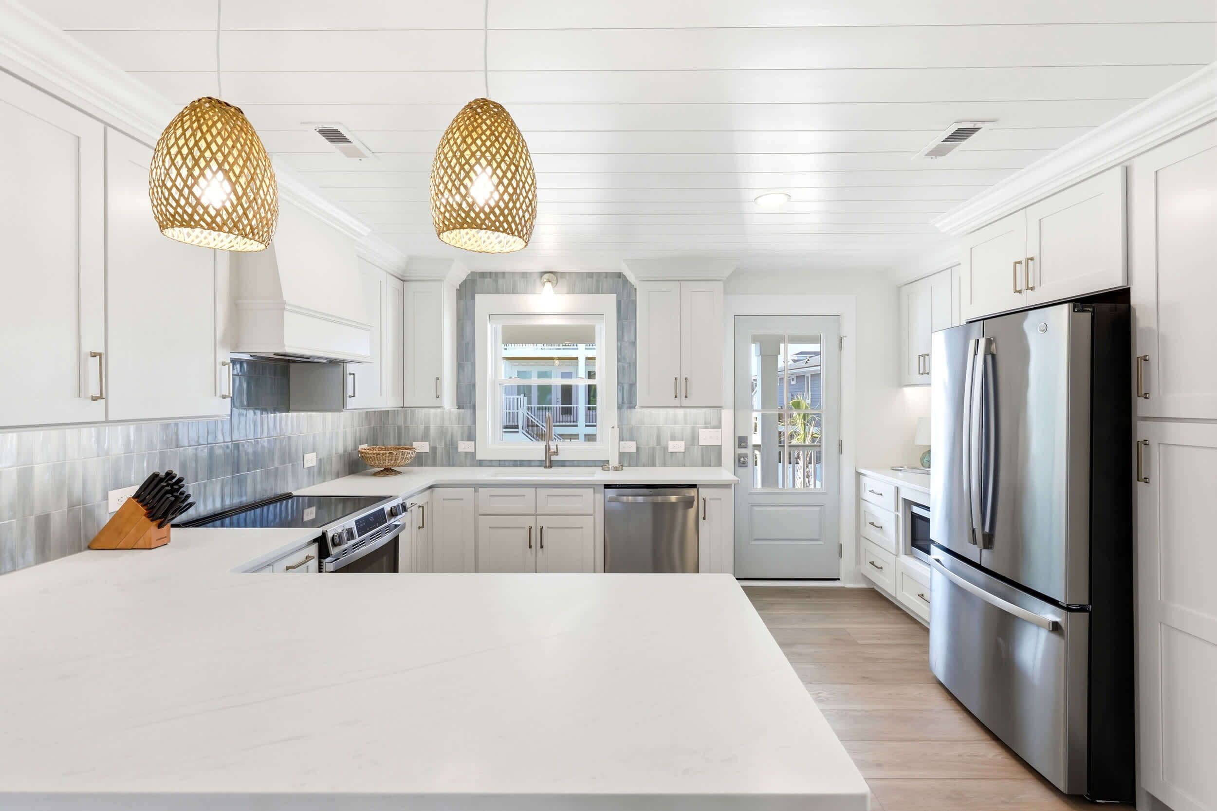 A modern kitchen with white cabinetry, a large island, stainless steel appliances, and pendant lighting.