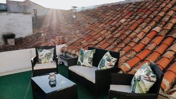 Une terrasse sur le toit, aménagée avec des meubles en osier, une table en verre et offrant une vue sur les toits en tuiles de couleur terre cuite.