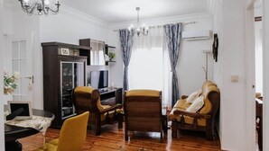 Ein Wohnzimmer mit Holzboden, einem Fernseher, einem Schreibtisch und zwei Sesseln.
