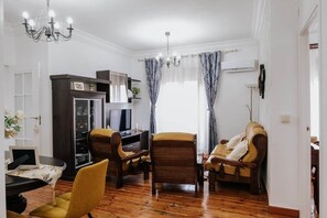 A living room with a wooden floor, a television, a desk, and two armchairs. - El Puente Grande Country House · Pool and Garden (Navahermosa)