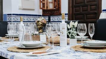 Une table à manger dressée avec des assiettes, des verres et une bouteille de vin, le tout surmonté d’un mur recouvert de carreaux bleus et blancs.