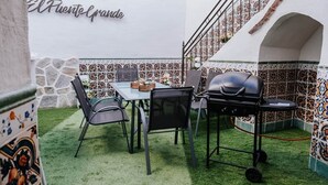 Eine Terrasse im Freien mit Tisch, Stühlen, einem Grill und einer Wand mit dekorativen Fliesen.