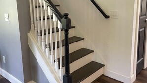 Eine Treppe mit weißen Balustern und dunklen Stufen, die zu einer Tür führt, an deren Wand ein kleines dekoratives Element angebracht ist.