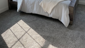 Ein Schlafzimmer mit einem Bett, großen Fenstern und Blick auf Bäume.