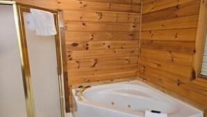 Ein Badezimmer mit Holzwänden, einer weißen Badewanne und einer Duschkabine aus Glas.