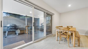 Zona de pati amb taula i cadires, una barbacoa i una porta corredissa de vidre que dona a un espai exterior.