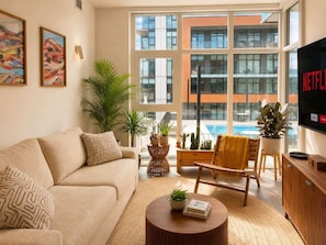 A modern living room with a sofa, armchair, coffee table, and a TV displaying Netflix. - Paloma | Resort-Style Lakeshore Condo with Pool (Kelowna)