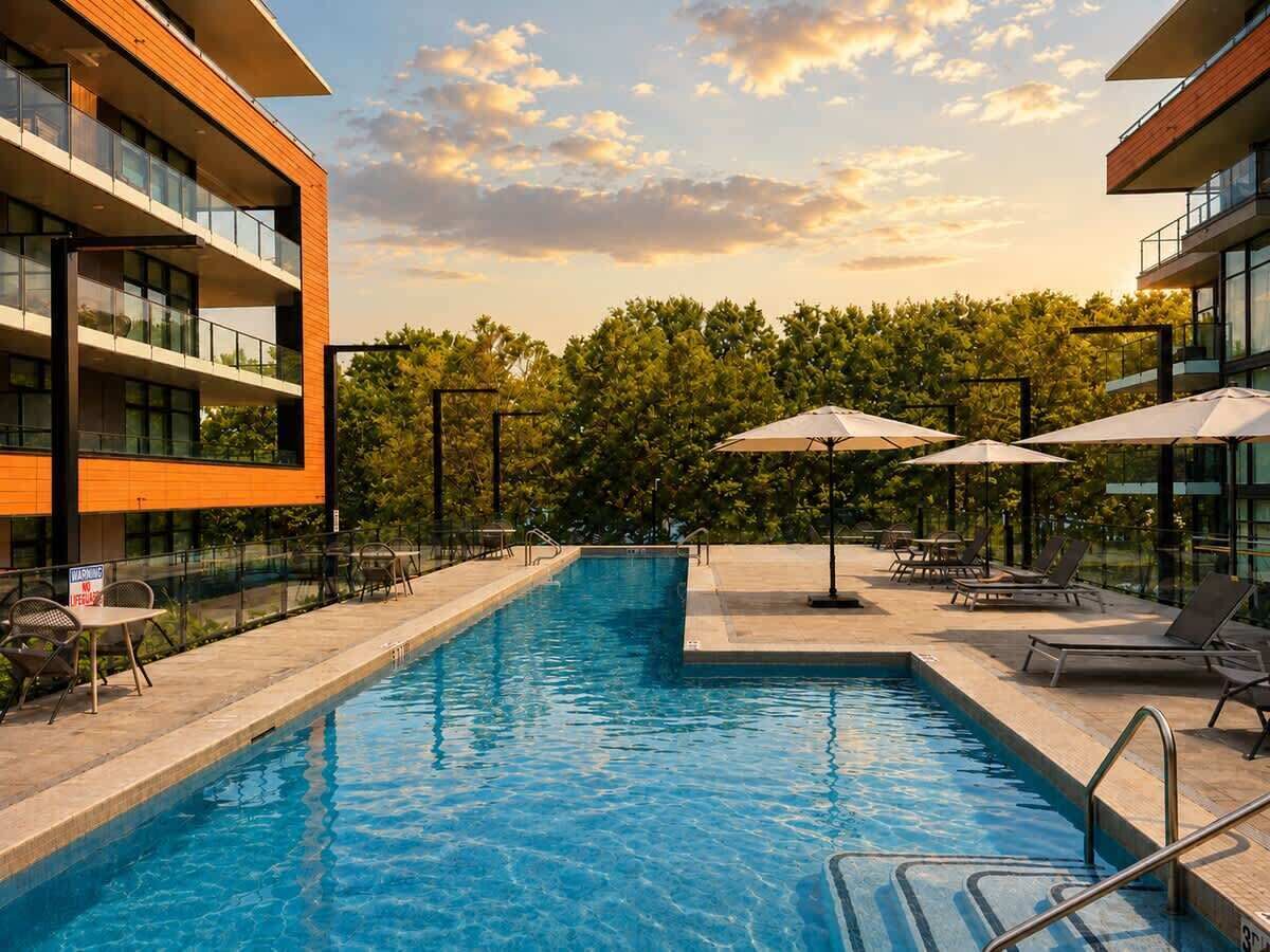 Une piscine entourée de bâtiments modernes et d’arbres, avec des chaises longues et des parasols.
