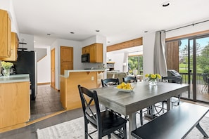 A modern kitchen with wooden cabinets, a central island, and a dining area with a table and chairs. - New Listing! Peaceful 3-bedroom condo in Stowe - access to the Rec Path and more (Stowe)