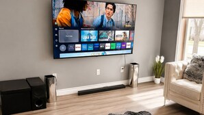 Una sala de estar con una televisión de pantalla plana montada en la pared, una alfombra mullida, un sofá, una mesa de centro y un altavoz.