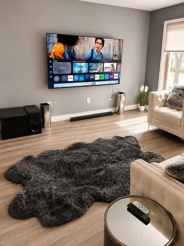 Un salon avec un téléviseur à écran plat fixé au mur, un tapis moelleux, un canapé, une table basse et un haut-parleur.