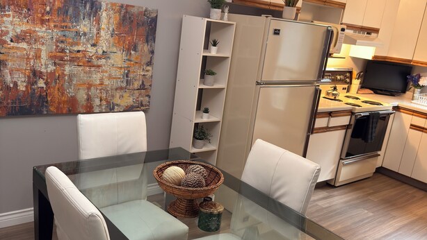 Una cocina moderna con una mesa de comedor de vidrio, sillas blancas, un refrigerador, una estufa y un televisor.