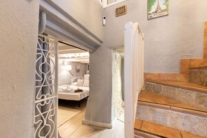 Un corridoio che conduce a una camera da letto con un letto, una scala con piastrelle decorate e un quadro appeso al muro raffigurante la Torre Eiffel.