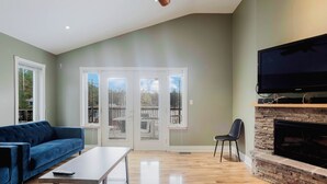 A living room with a blue sofa, a coffee table, a fireplace, a television, and a sliding glass door leading to an outdoor deck. - 4 Bedroom Main Cottage XIV: PL (Gravenhurst)