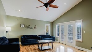 A living room with a ceiling fan, two dark sofas, a coffee table, and large windows with blinds. - 4 Bedroom Main Cottage XIV: PL (Gravenhurst)