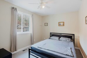 Ein Schlafzimmer mit einem Bett, einem Deckenventilator, einem Fenster mit Vorhängen und zwei gerahmten Bildern an der Wand.