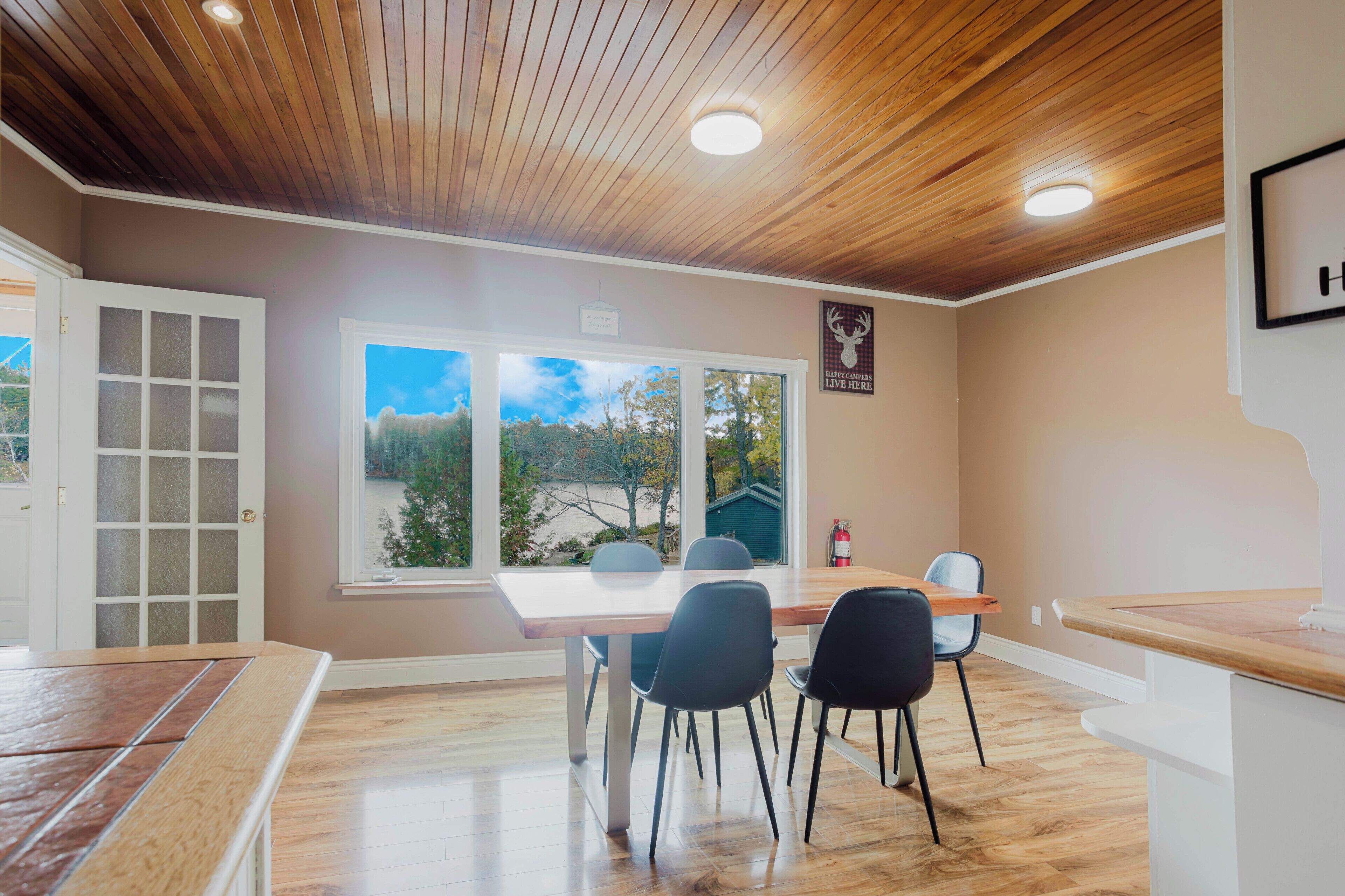 A dining area with a wooden ceiling, a large window with a view, and a sign on the wall.