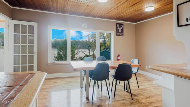 A dining area with a wooden ceiling, a large window with a view, and a sign on the wall. - 4 Bedroom Main Cottage XIV: PL (Gravenhurst)