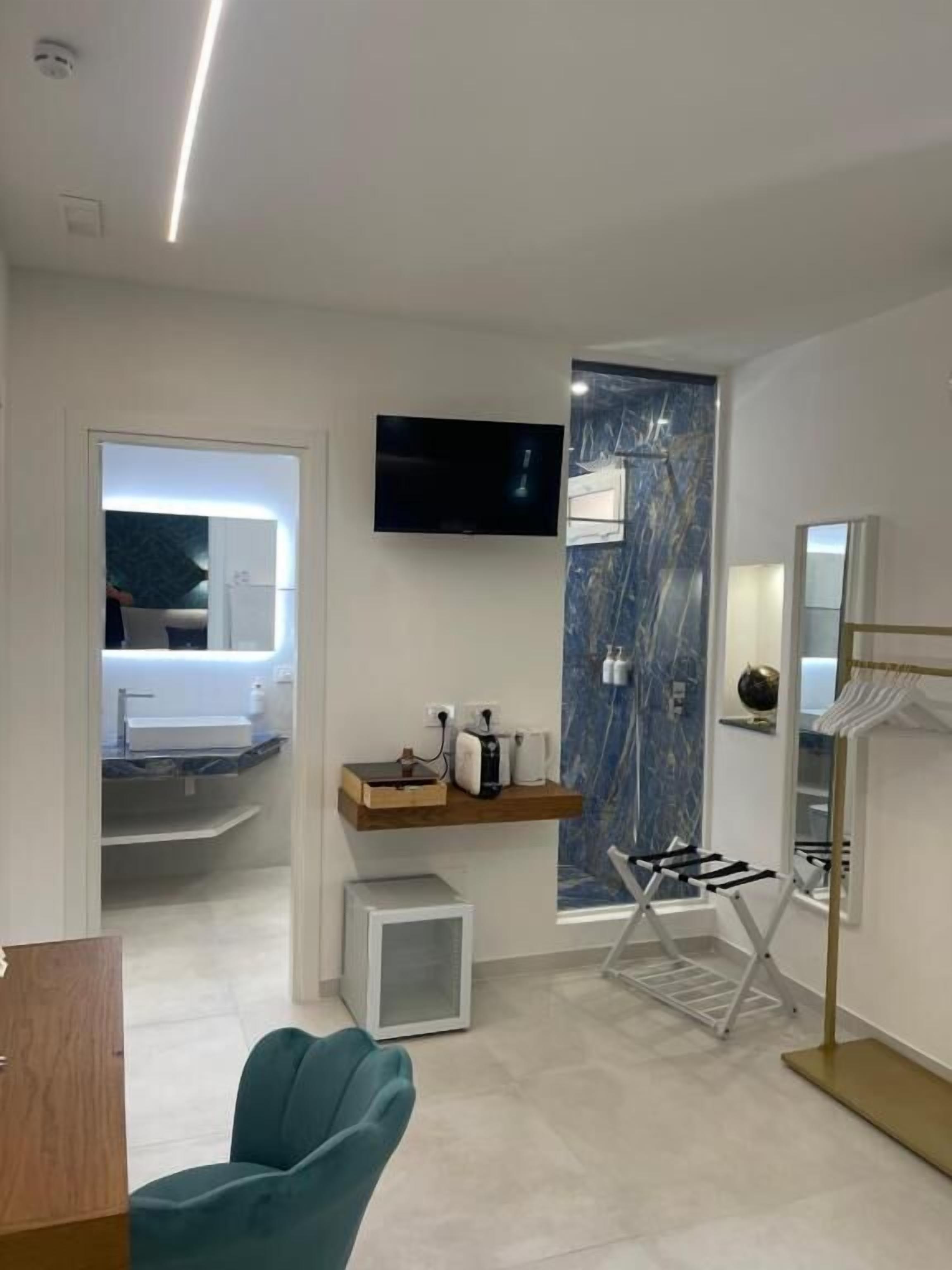 Une chambre d’hôtel moderne dotée d’une télévision à écran plat, d’un mur décoratif en marbre, d’une coiffeuse intégrée et d’un coin salon avec un fauteuil turquoise.