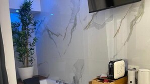 Un baño moderno con una bañera grande, un televisor montado y un estante de madera con artículos de aseo.