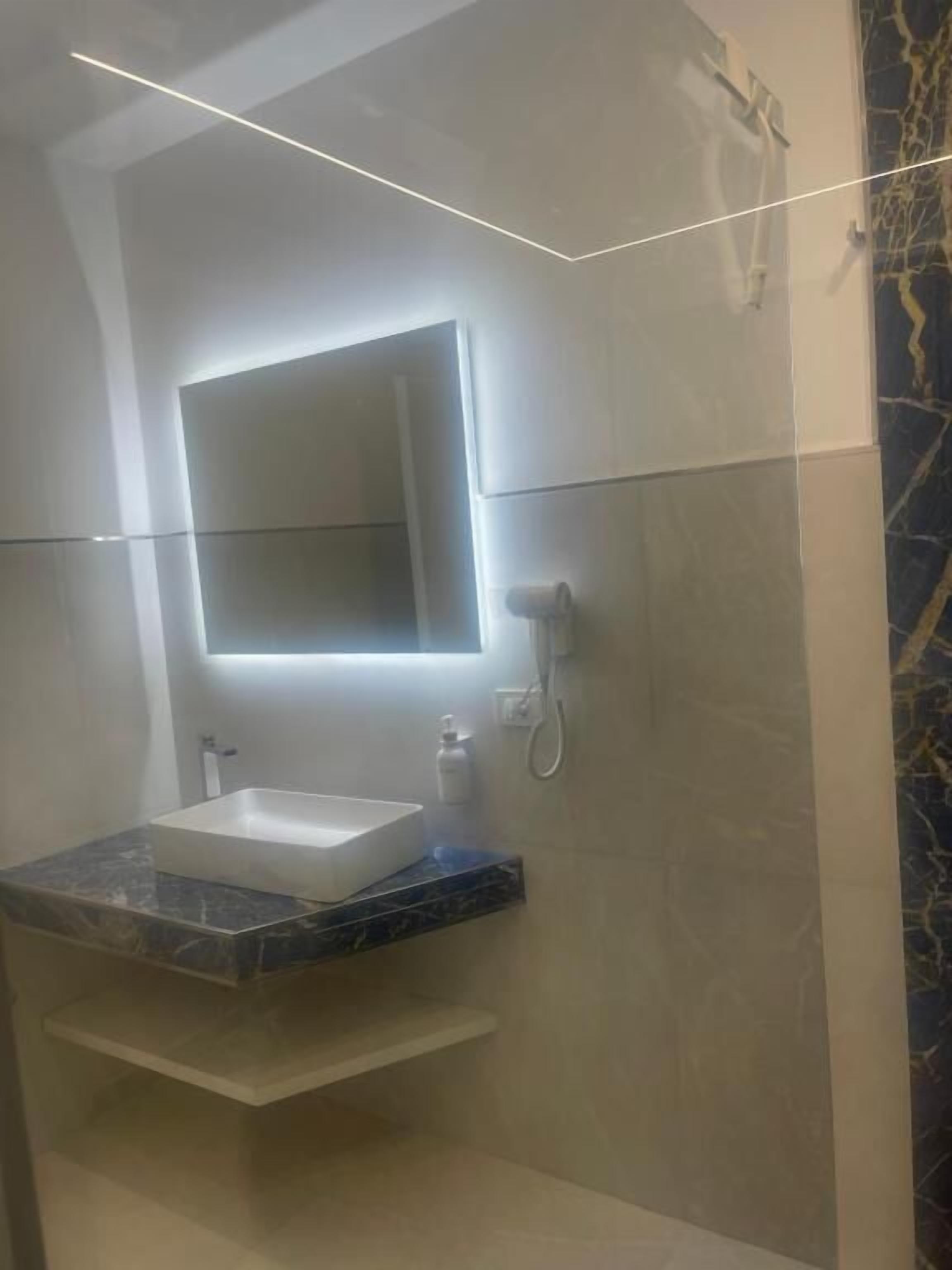 Un baño con un espejo rectangular, un lavabo blanco, encimera de mármol y zona de ducha.