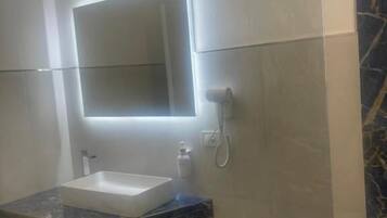 Un baño con un espejo rectangular, un lavabo blanco, encimera de mármol y zona de ducha.
