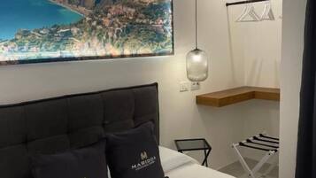 Une chambre d’hôtel avec une grande fenêtre, un lit avec deux oreillers, un luminaire suspendu, une étagère en bois et un étendoir.