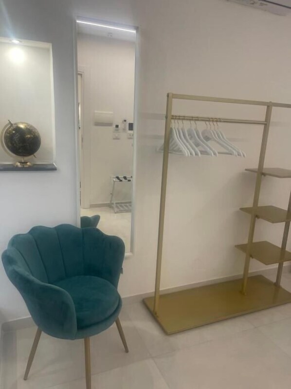 A teal chair, a gold-framed clothing rack, and a mirror on the wall.