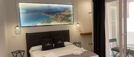 Un dormitorio con una cama grande, vista a un paisaje costero, puerta corrediza de vidrio y una lámpara colgante.