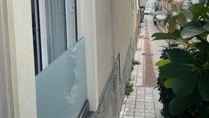Una calle urbana estrecha flanqueada por edificios, con aceras de baldosas y algo de vegetación.